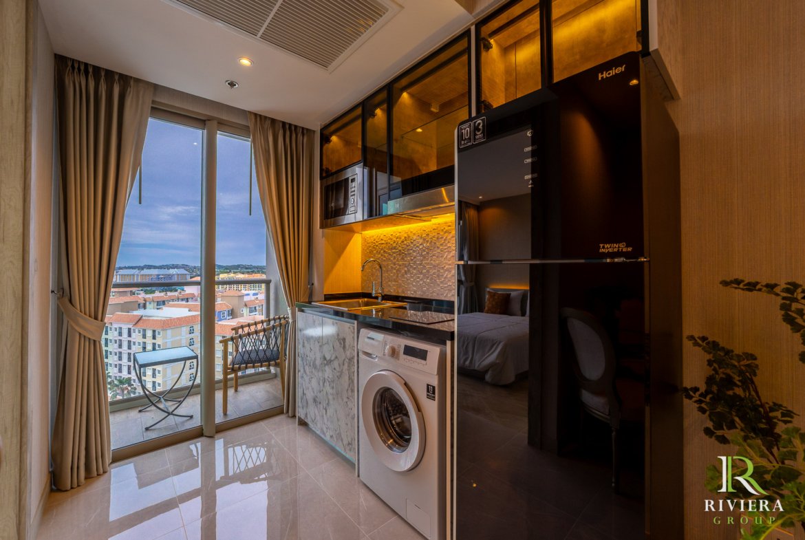 Modern kitchen with built-in microwave, fridge and washing machine beside glass balcony doors overlooking a cityscape.