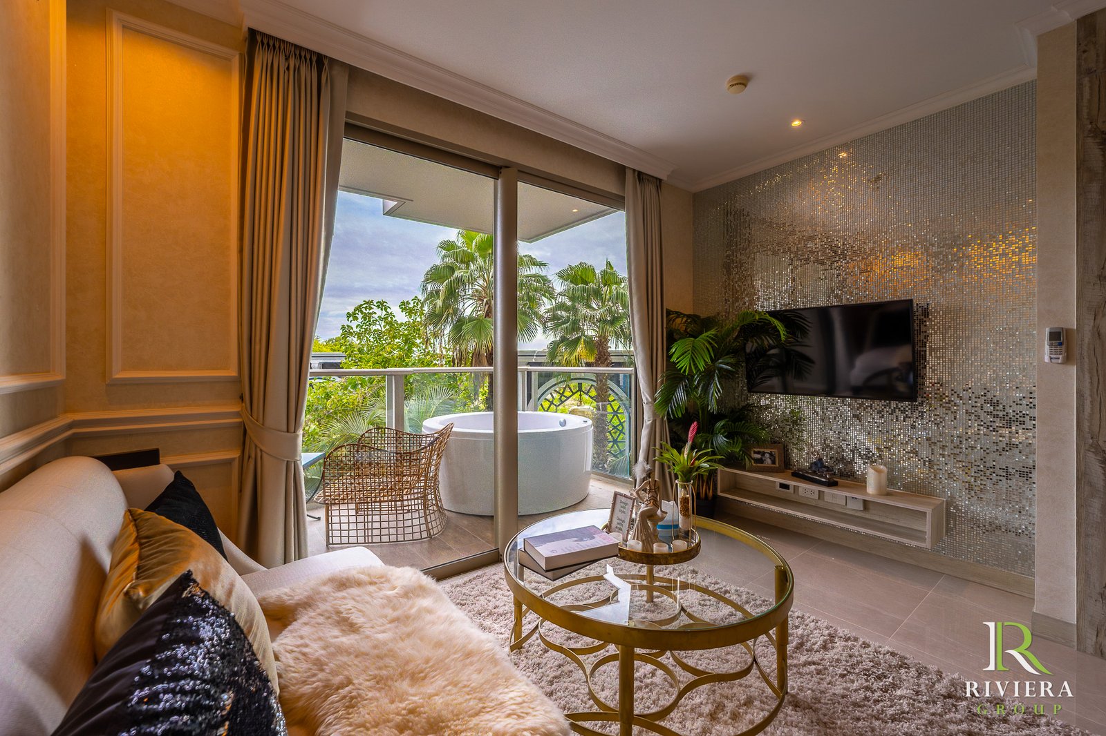 302-S07 Luxurious living room with glass doors opening to a tropical balcony, palm trees outside, and a mosaic-tiled wall with a mounted TV on the right.