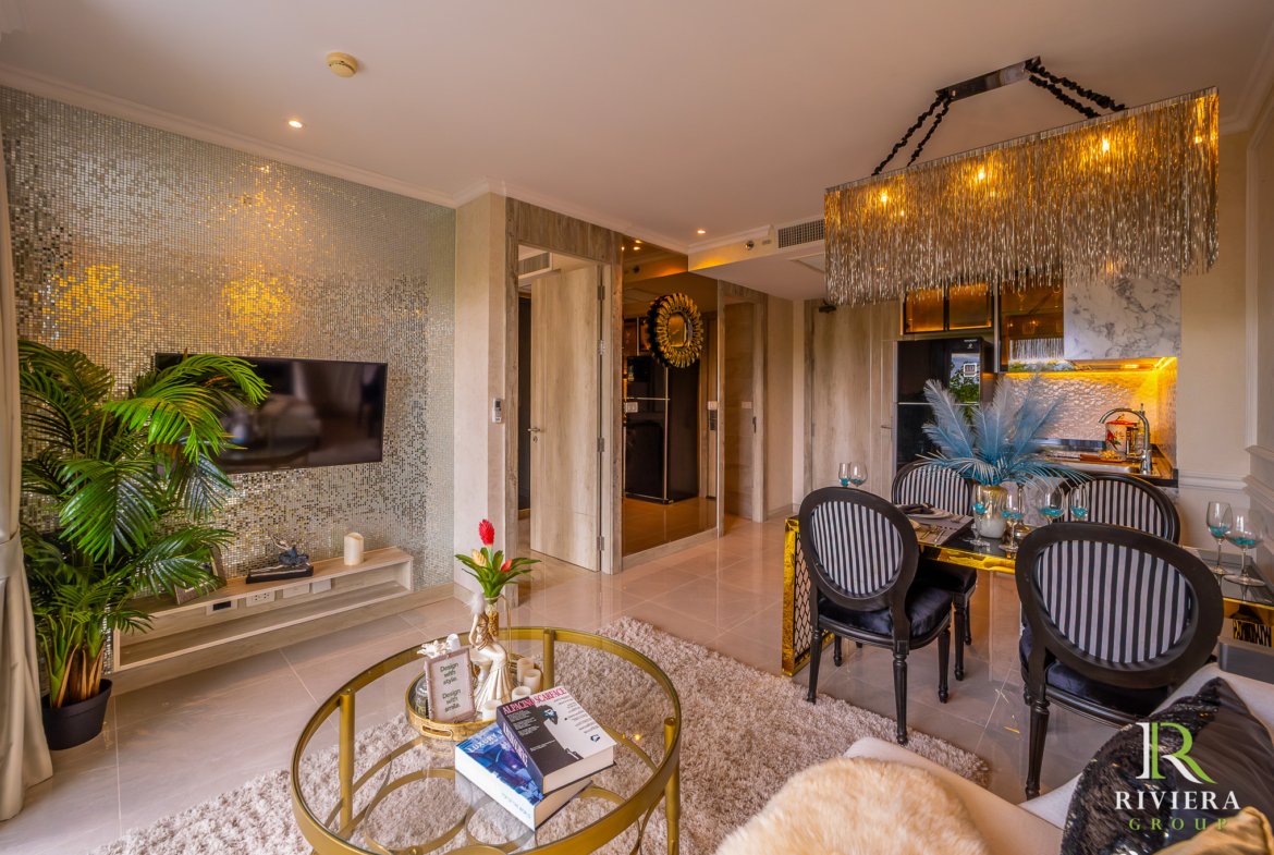 Luxurious living and dining area with a mosaic wall, glass coffee table, green plants, and a gold-fringed chandelier above the dining set.