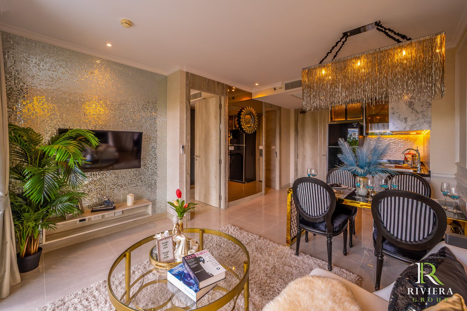 302-S08 Luxurious living and dining area with a mosaic wall, glass coffee table, green plants, and a gold-fringed chandelier above the dining set.