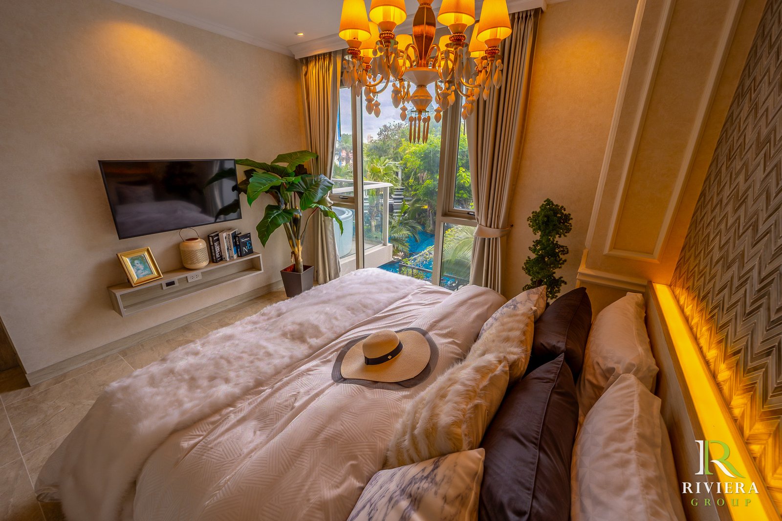 302-S12 Luxurious hotel bedroom with a chandelier, beige walls, a plush bed, and a large window overlooking greenery outdoors.