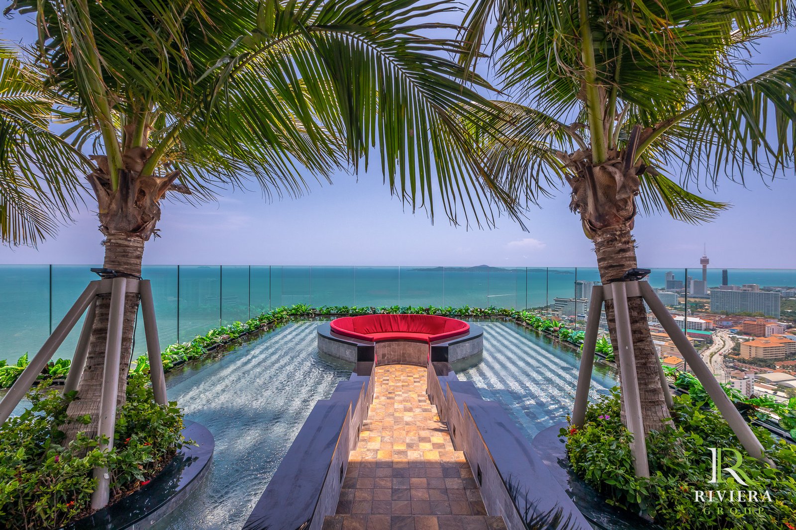 347582729_976407183353544_1187333440121853701_n Rooftop pool with a red circular seating area, palm trees, and a glass barrier overlooking a coastal city skyline.