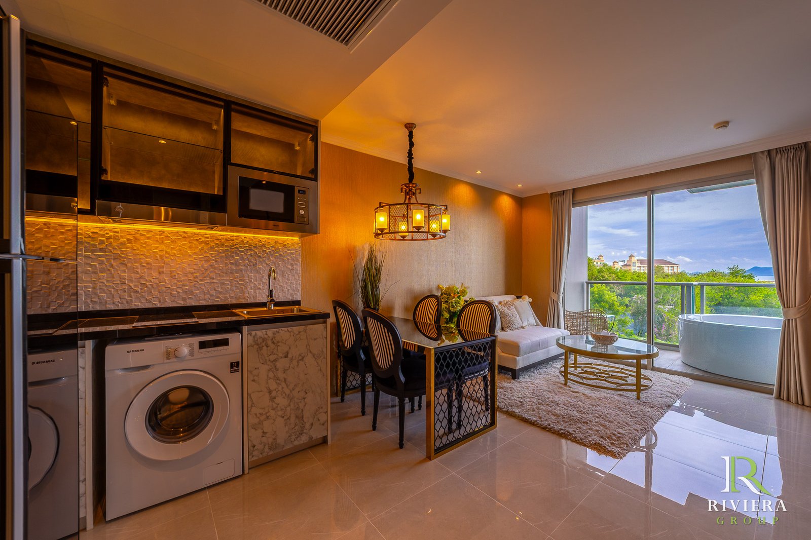 502-S02 Open-plan kitchen and living area with stainless steel appliances, a dining table, chandelier, and a balcony view of trees and buildings.