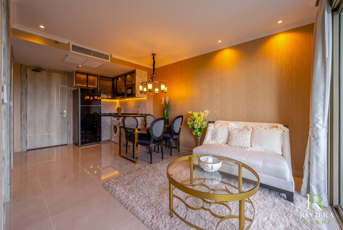 Open-plan living area with a dining table, kitchen, and cream sofa, featuring a gold textured wall and warm pendant lighting above the dining table.