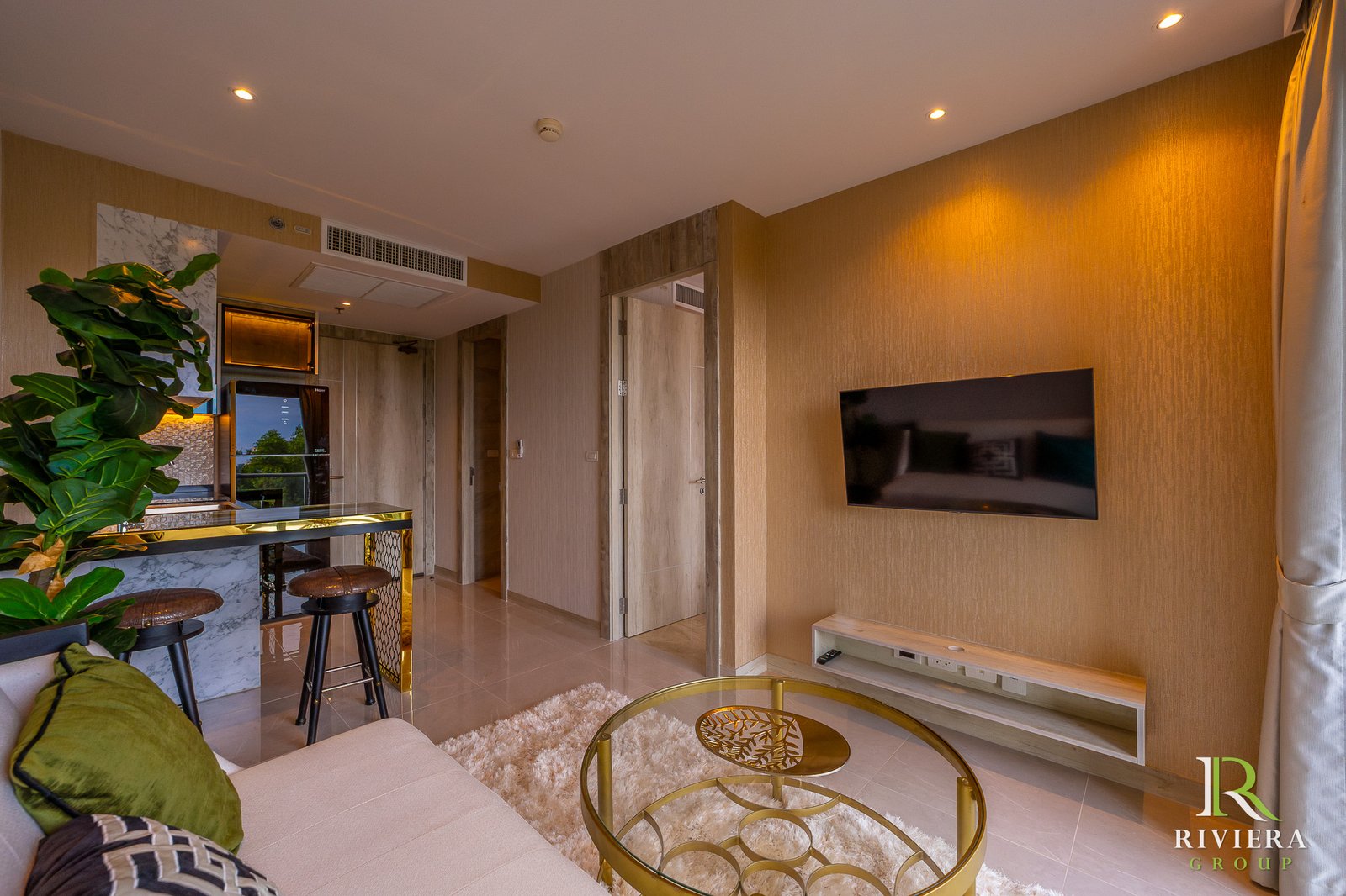 Modern living room with a wall-mounted TV on a textured brown wall, glass coffee table, and a fluffy white rug.