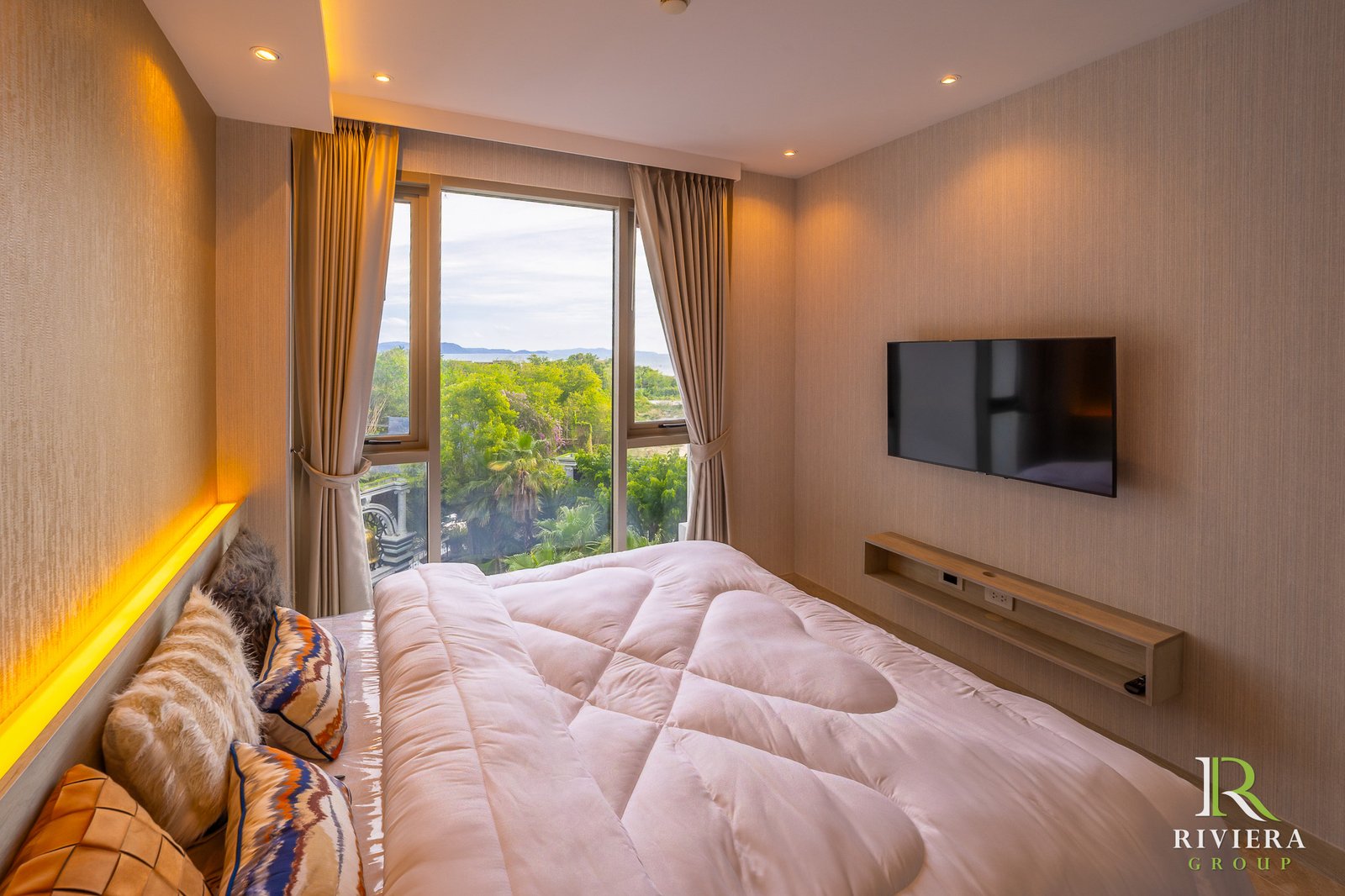505-S10 Hotel bedroom with a large window and view of trees and water, pink comforter, and wall-mounted TV on the right.