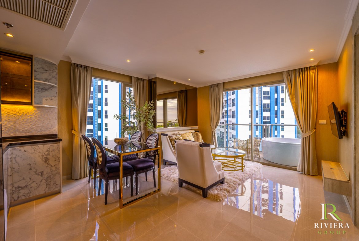 Luxurious living room with a glass dining table, dark chairs, beige curtains, and large windows overlooking a city skyline.
