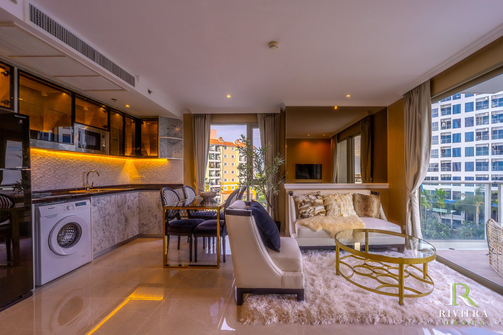 Open-plan living area with a marble kitchen, bar seating, and a fluffy white rug, large windows overlook a cityscape.