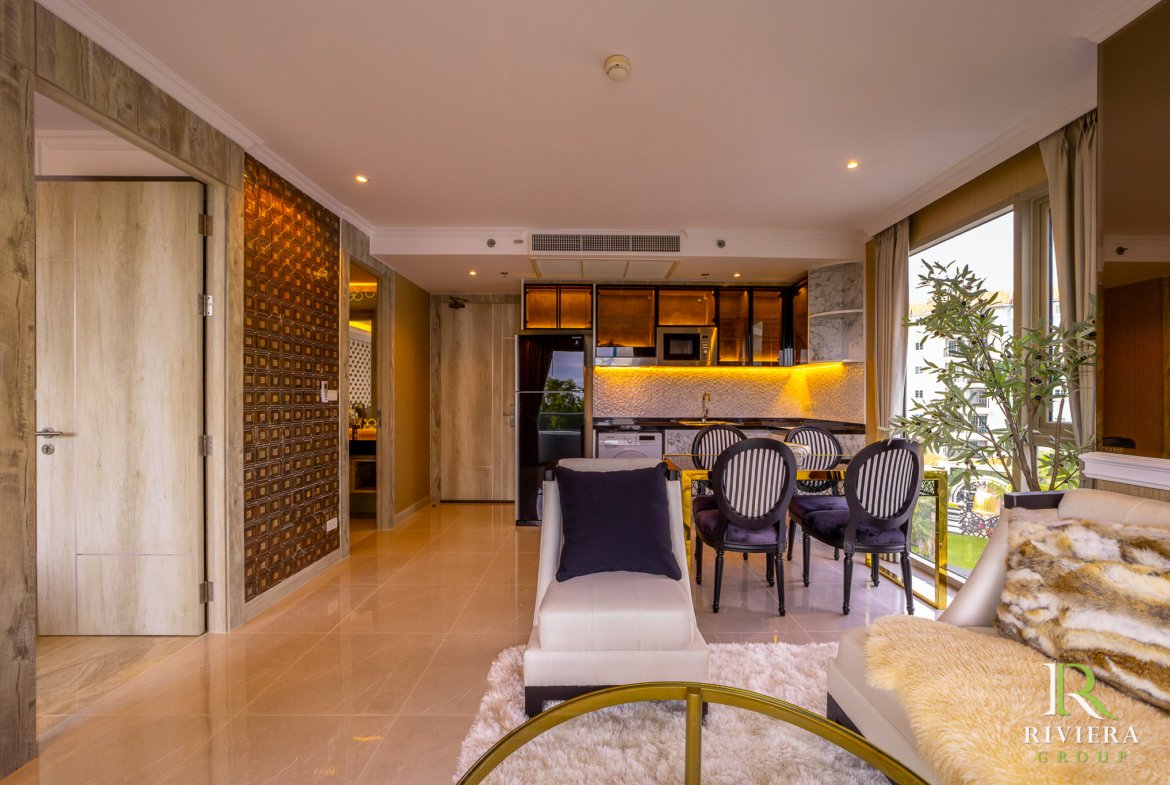 Open-plan living area with a beige tiled floor, kitchen island, and large windows with a potted tree nearby.
