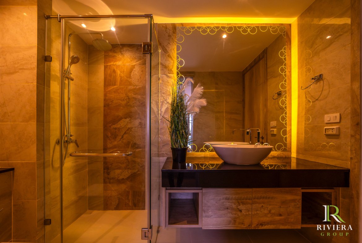 Luxurious marble bathroom with a glass shower, vessels sink, and a mirror featuring a yellow circular pattern.