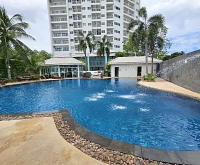 Curved blue pool at a resort with palm trees, lounge chairs, and a tall building in the background.