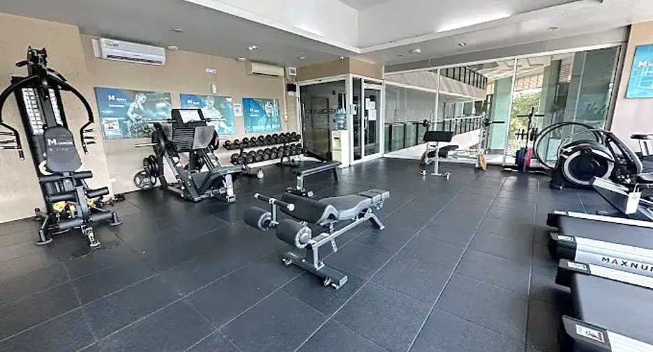 Modern gym interior with multiple workout machines, free weights, and cardio equipment across a dark tiled floor.
