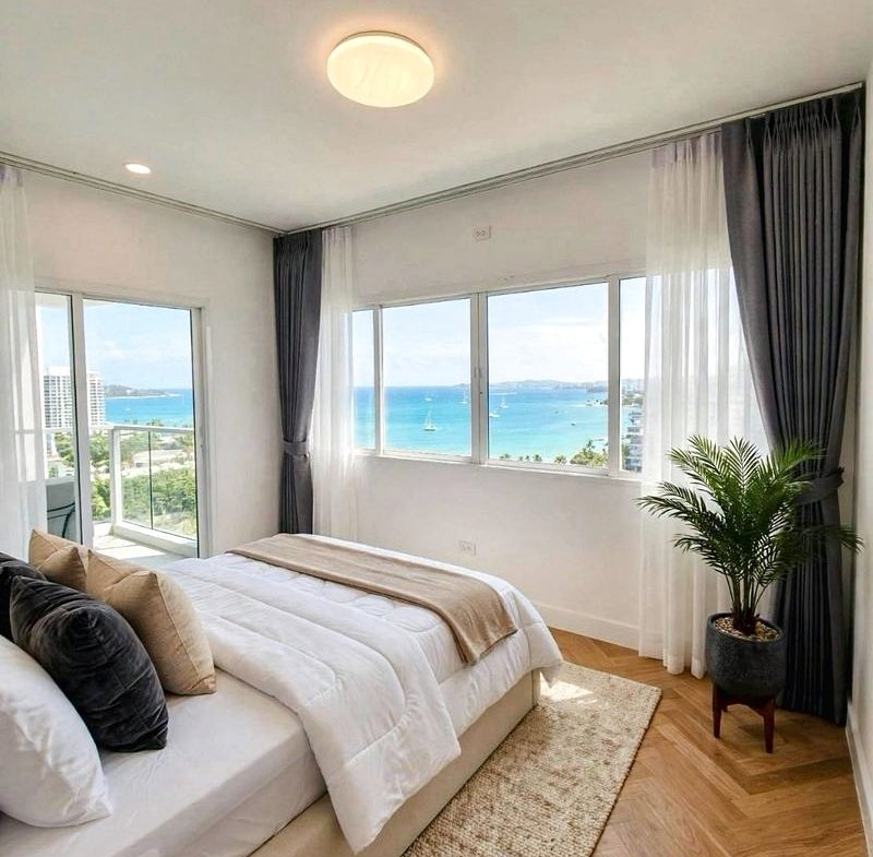 Bright coastal bedroom with a large window overlooking the ocean, white bed and neutral decor.