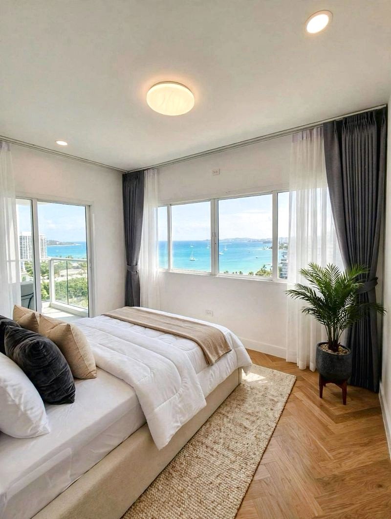 Bright coastal bedroom with a large window overlooking the ocean, white bed and neutral decor.