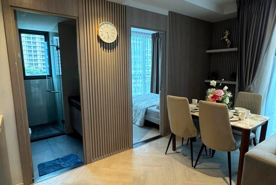 Dining area in a modern apartment with beige chairs, a marble table set for a meal, and glass windows with dark drapes; flower centerpiece on the table.