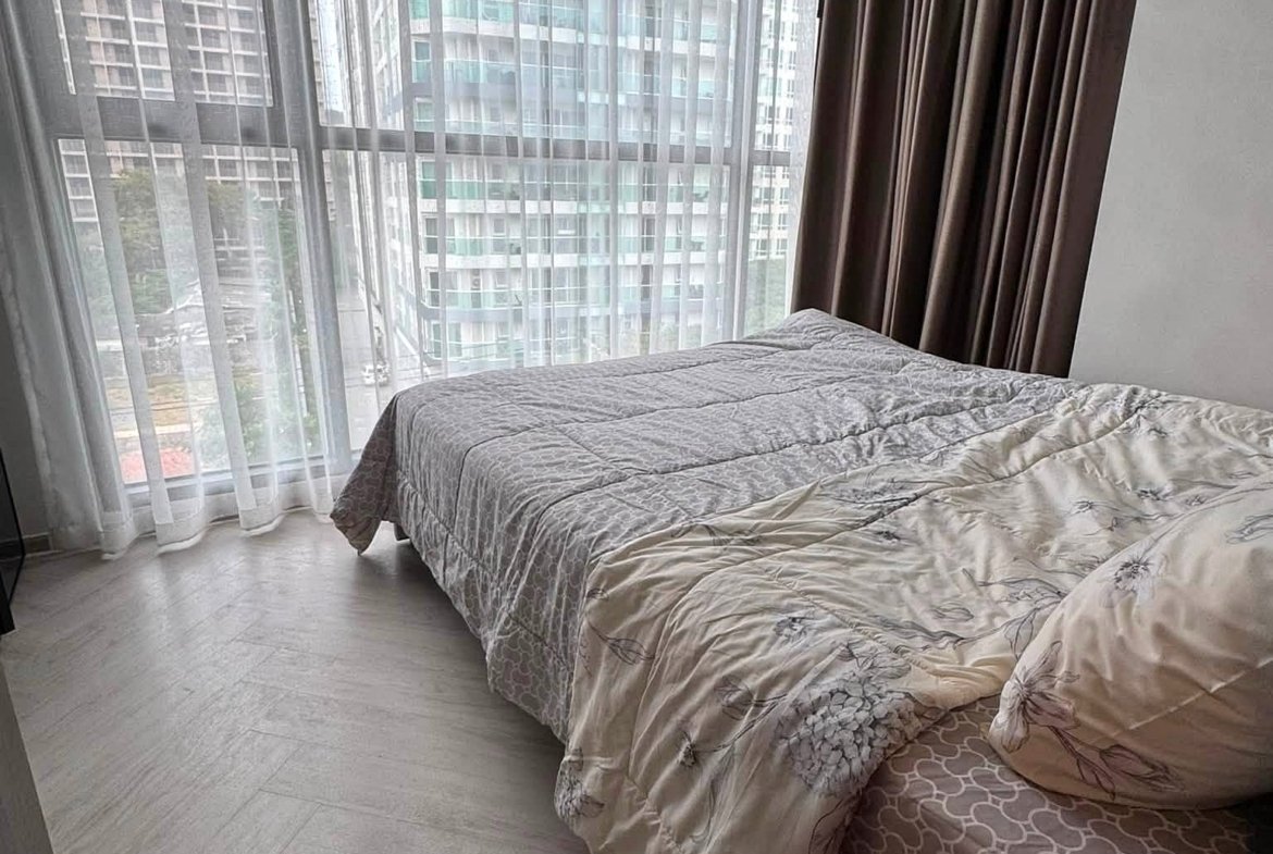 Bedroom with a large window wall, sheer white curtains, and a gray patterned comforter on a bed nearby.