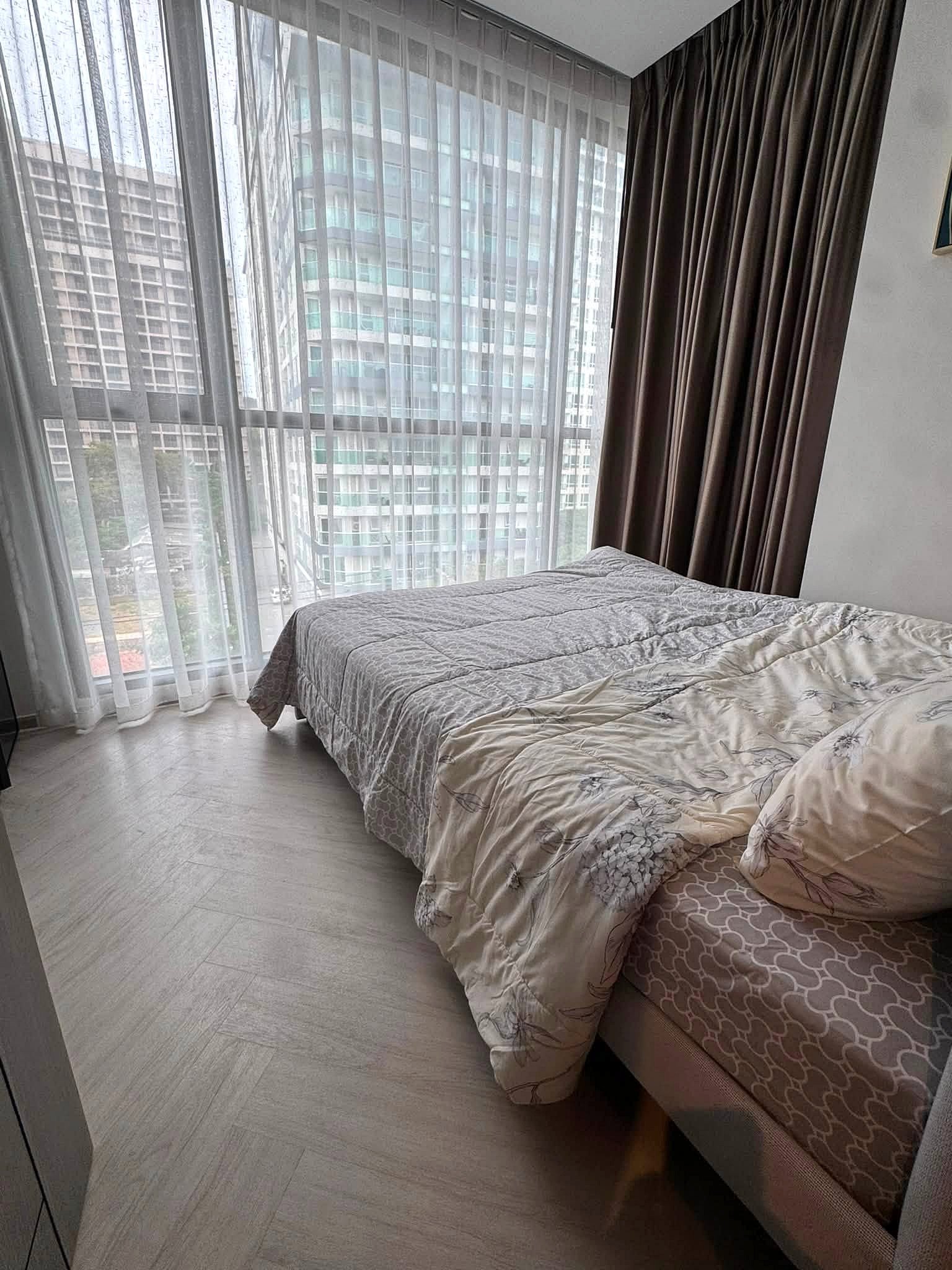 Andromeda_Pattaya_2Bed_Sale_Rent_Dlc631_5 Bedroom with a large window wall, sheer white curtains, and a gray patterned comforter on a bed nearby.
