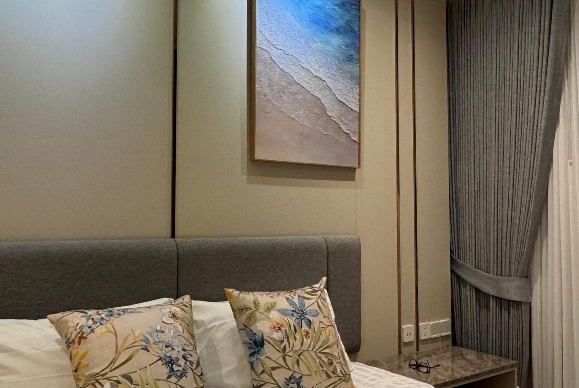 Hotel-style bedroom with a striped bedspread, floral throw pillows, and a beach-themed canvas on the wall.