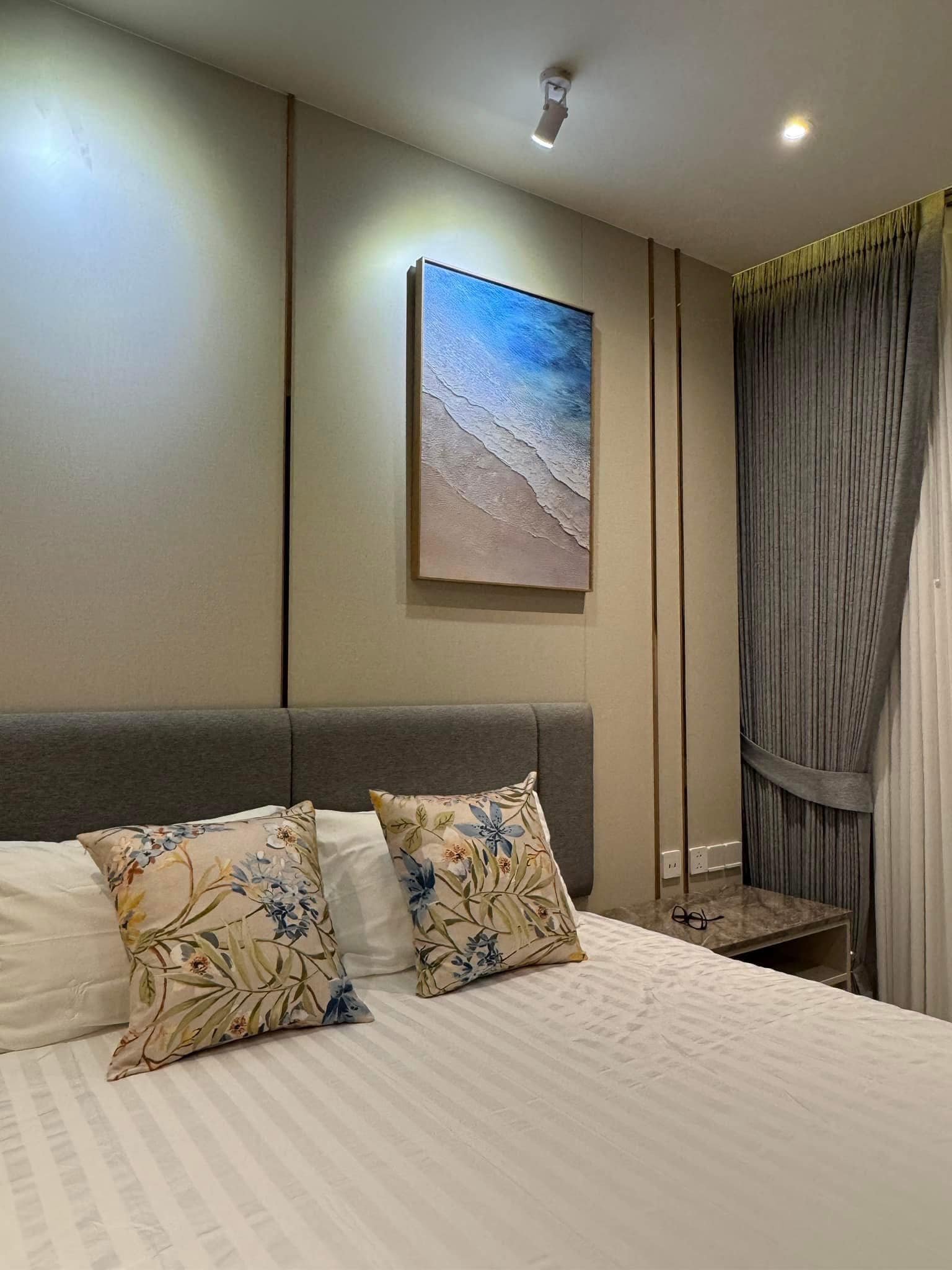 Arom_Wongamat_1005_3 Hotel-style bedroom with a striped bedspread, floral throw pillows, and a beach-themed canvas on the wall.