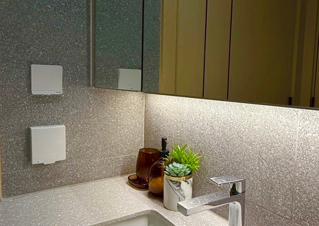 Modern bathroom vanity with a gray terrazzo countertop, undermount sink, and chrome faucet, plus a small succulent in a marble pot and brown glass bottles beside it.