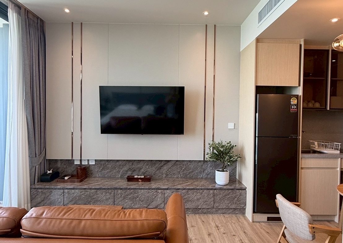 Living room with a wall-mounted TV above a marble console, brown leather sofa, and a potted plant nearby.
