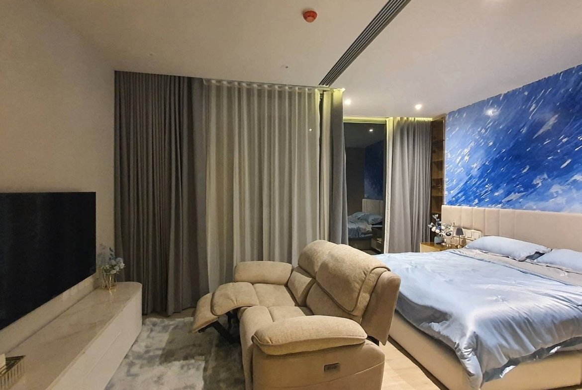 Hotel bedroom with a blue splash accent wall, a king bed with light blue sheets, and beige recliners nearby.