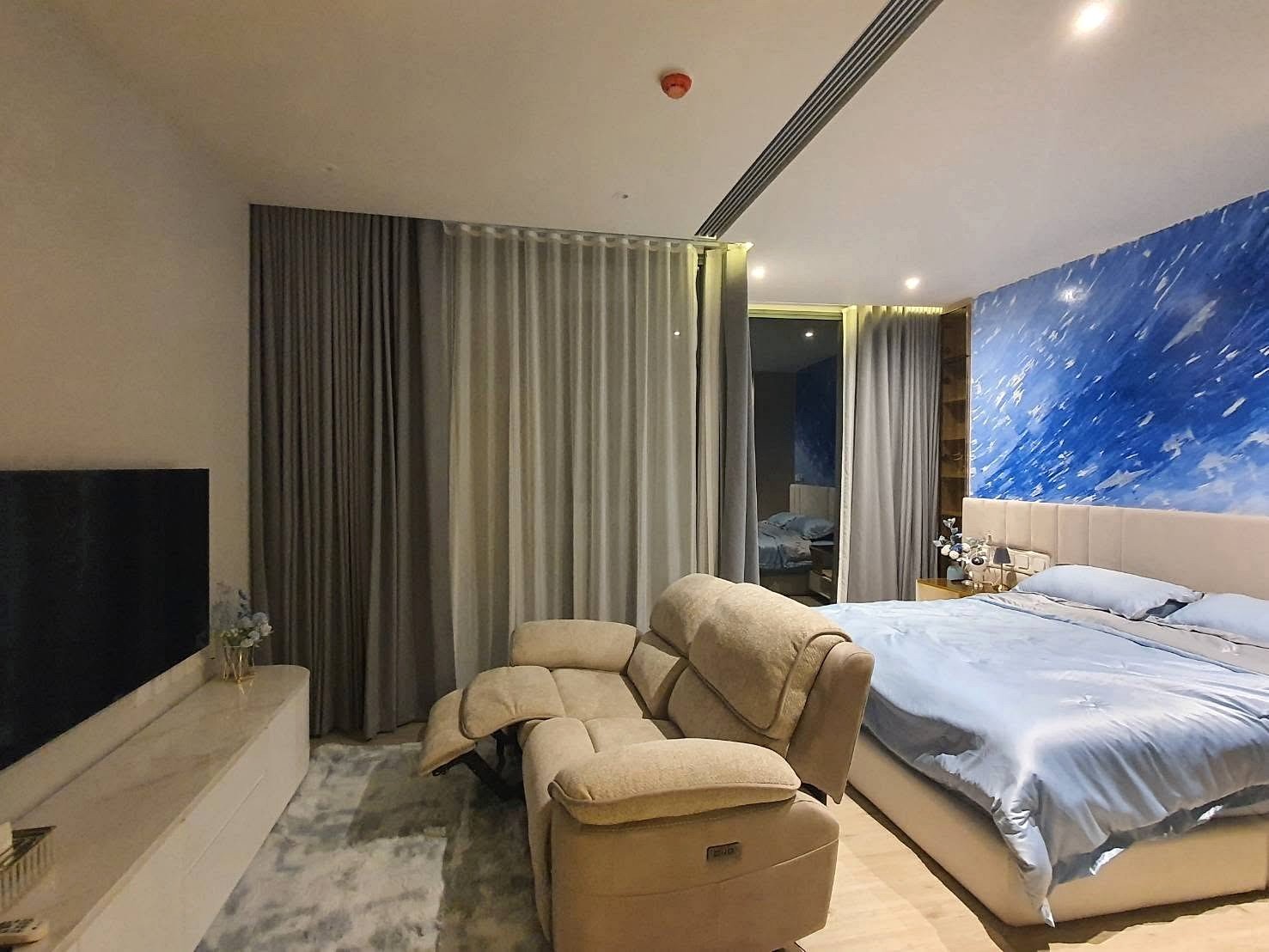 Arom_Wongamat_1bed_Rent_Rdl334 Hotel bedroom with a blue splash accent wall, a king bed with light blue sheets, and beige recliners nearby.