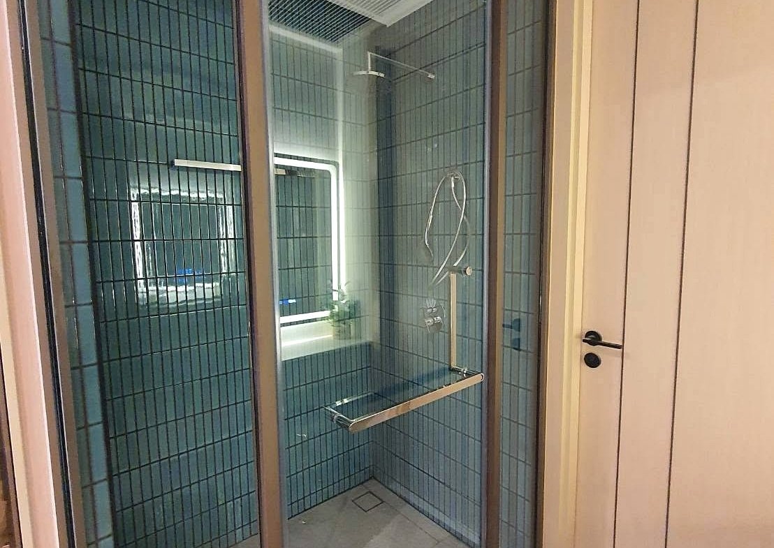 Glass-walled shower enclosure with blue tile walls and a chrome grab bar inside the bathroom. Jeans? (A concise description: modern shower stall with blue-tiled walls and metal fixtures.)