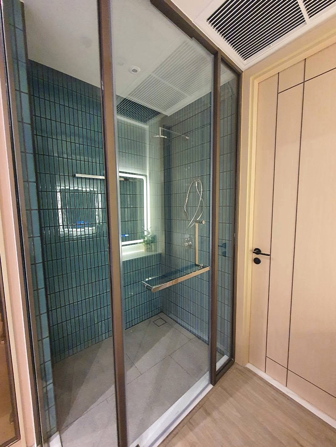 Arom_Wongamat_1bed_Rent_Rdl334_11 Glass-walled shower enclosure with blue tile walls and a chrome grab bar inside the bathroom. Jeans? (A concise description: modern shower stall with blue-tiled walls and metal fixtures.)
