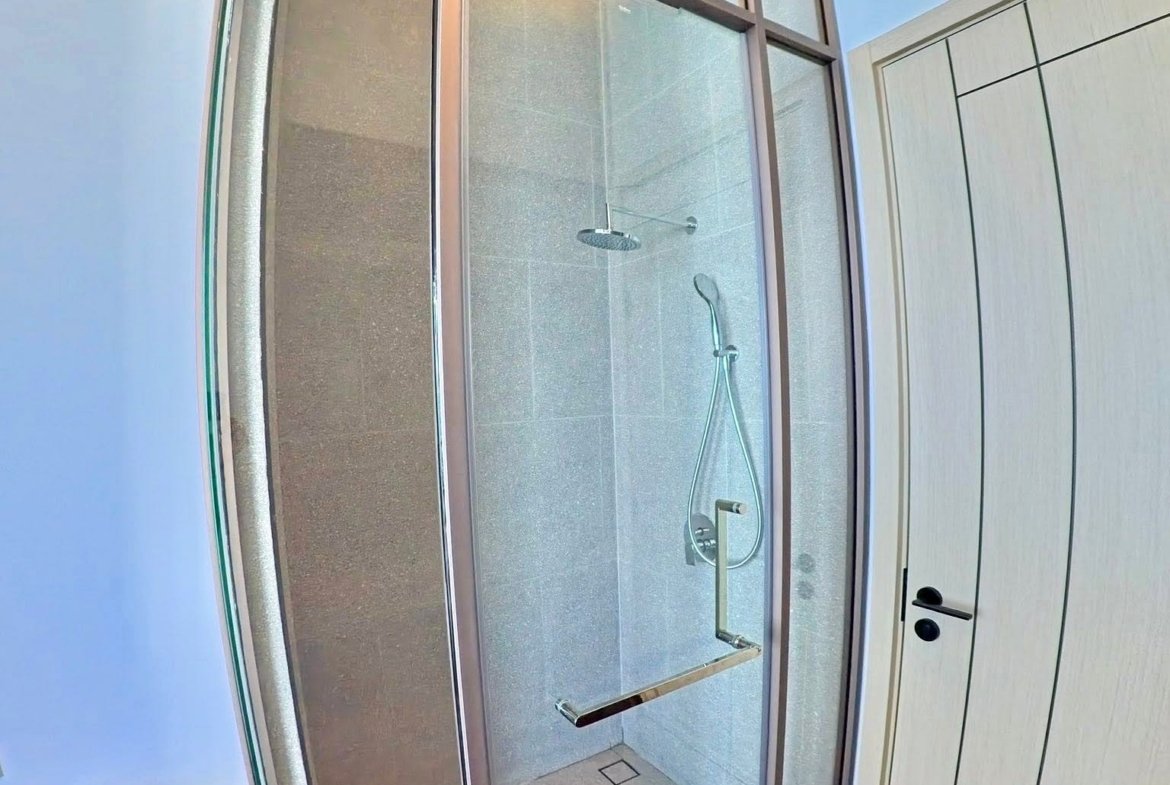 Modern glass shower enclosure with metal frame, viewed from doorway, showing a rainfall showerhead and handheld shower inside.