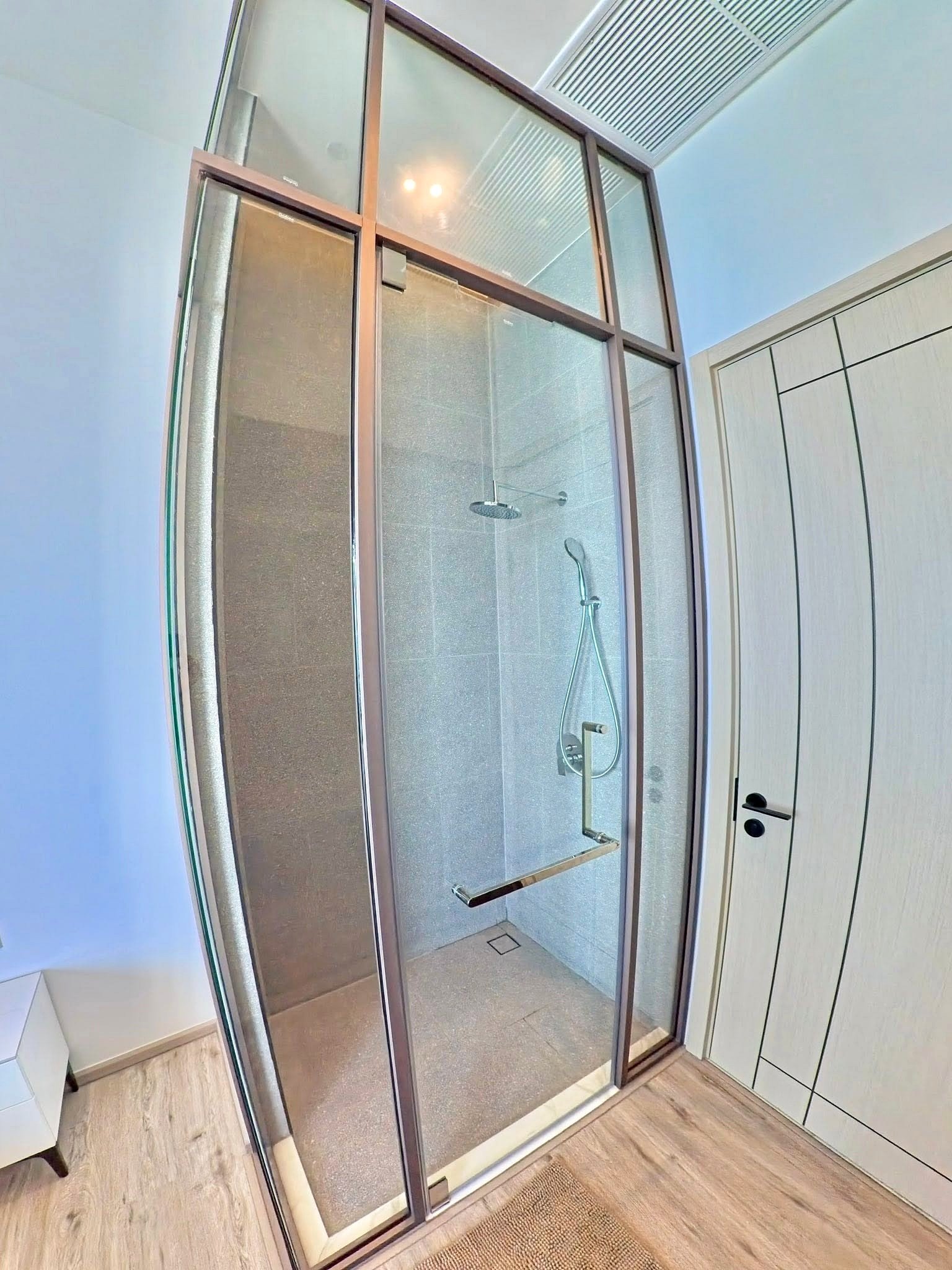 Arom_Wongamat_5005_10 Modern glass shower enclosure with metal frame, viewed from doorway, showing a rainfall showerhead and handheld shower inside.