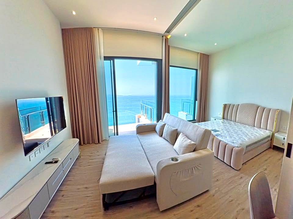 Hotel suite living area with a beige sofa, TV, and ocean-view balcony doors.