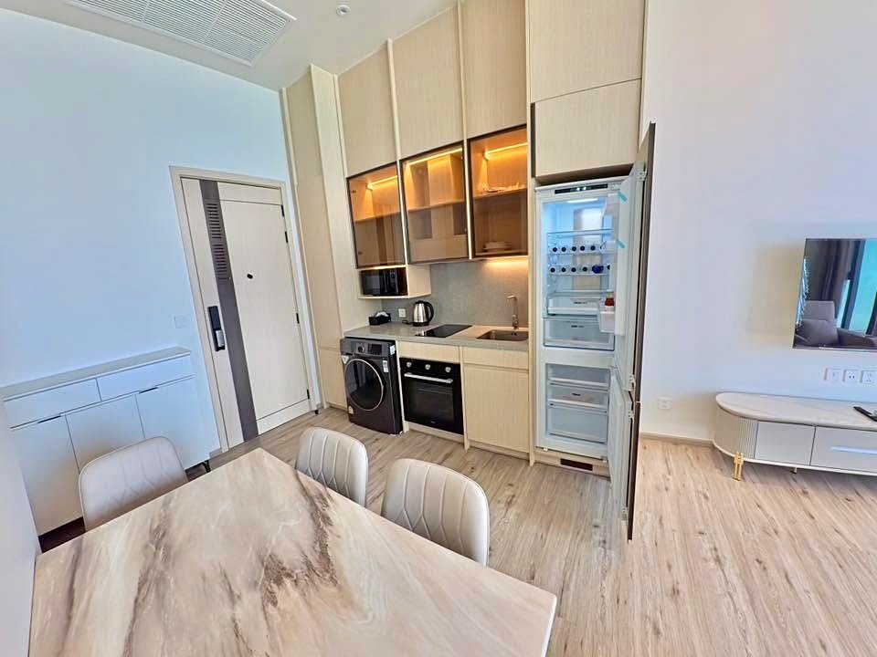 Open refrigerator in a modern kitchen with built-in oven, washing machine, and marble dining table in the foreground to the left.