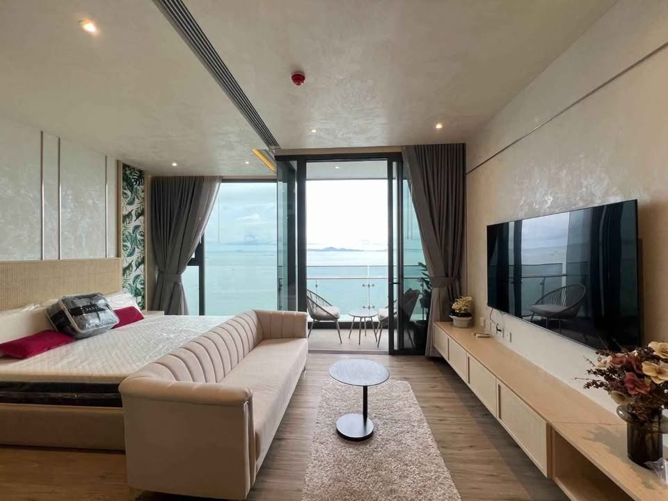 Luxury hotel suite with a king bed, cream sofa, and wall-mounted TV facing a sea-view balcony.