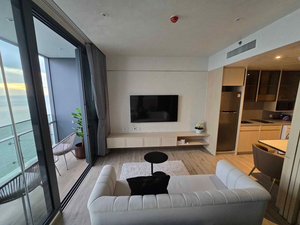 Contemporary living room with a white sofa facing a wall-mounted TV and a low white media console, balcony with an ocean view.