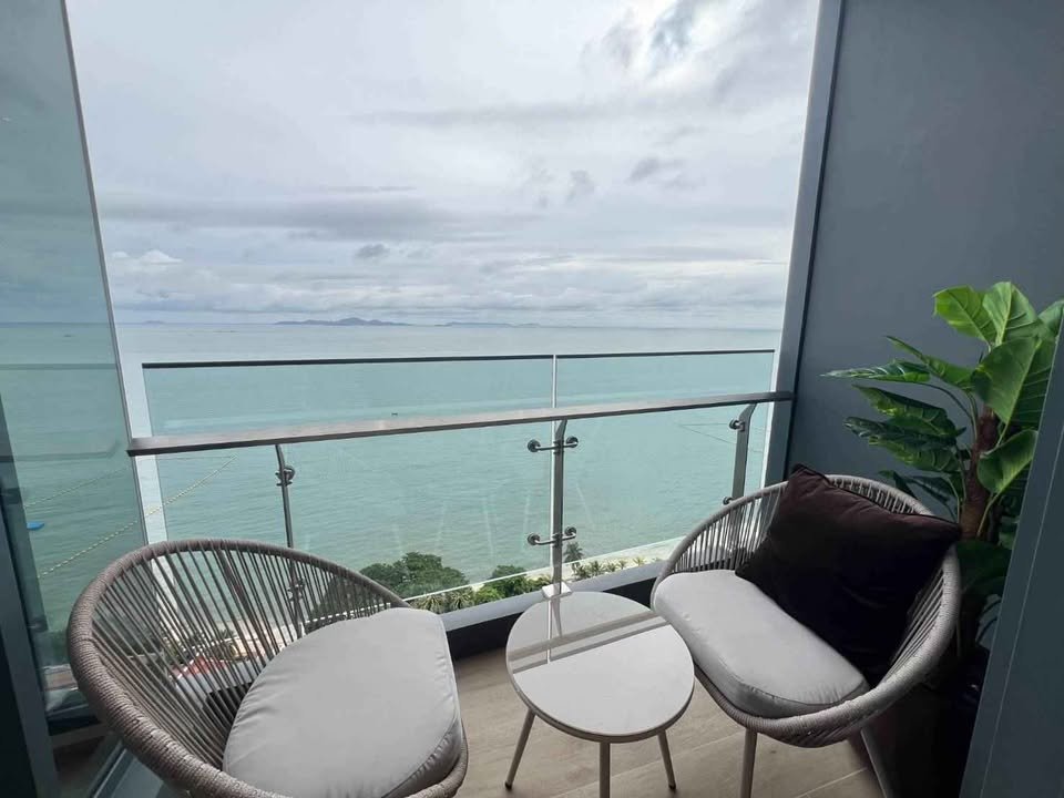 Balcony with two round wicker chairs and a small table, overlooking a turquoise sea and cloudy sky.