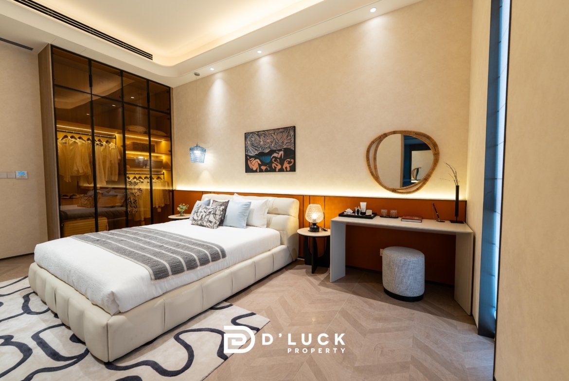 Luxurious hotel bedroom with a king-size bed, beige walls, and a glass-front wardrobe on the left side.