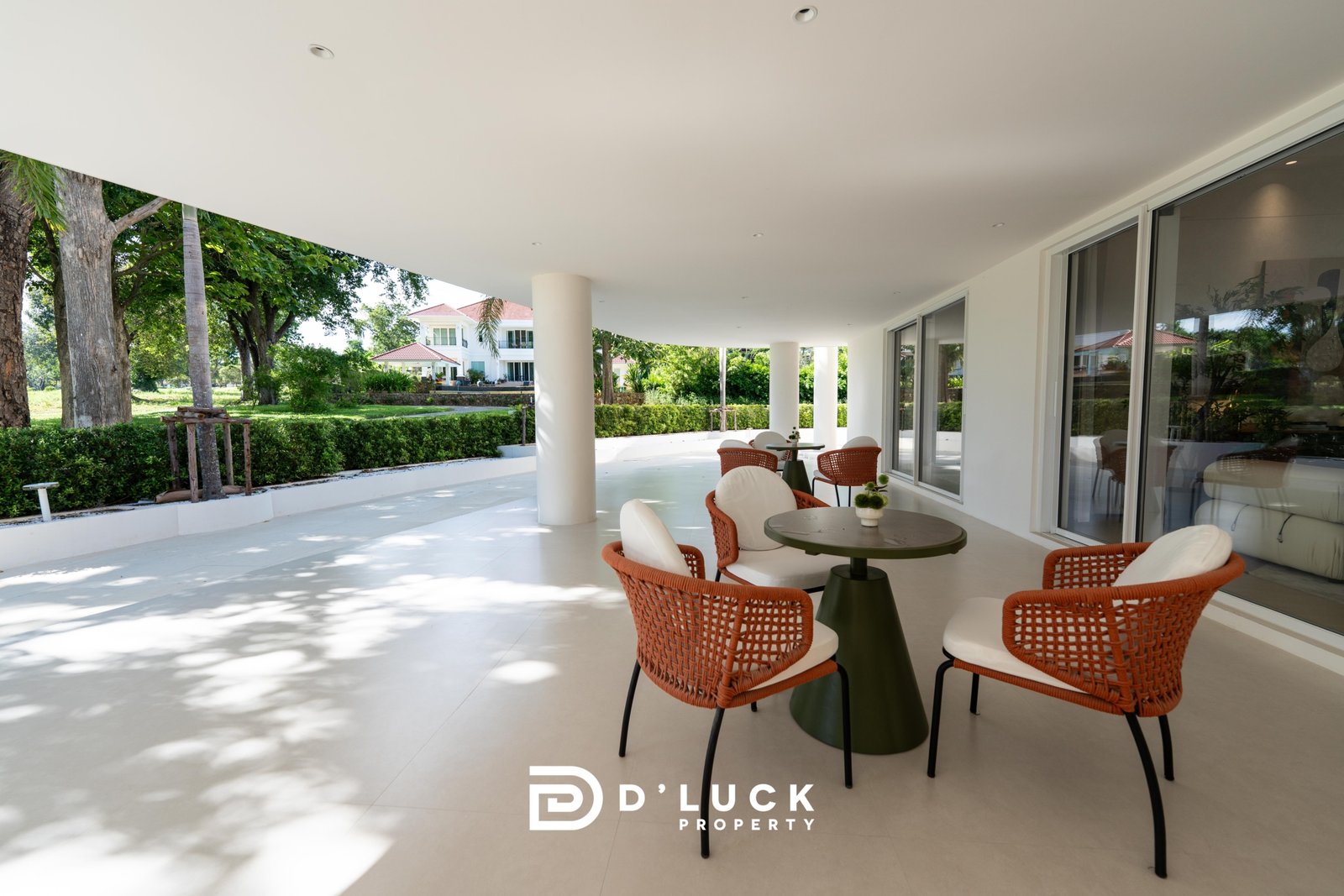 Big_V_Pattaya_Type_A_125 Covered outdoor seating area with orange wicker chairs around round green tables, next to glass sliding doors and a landscaped garden.