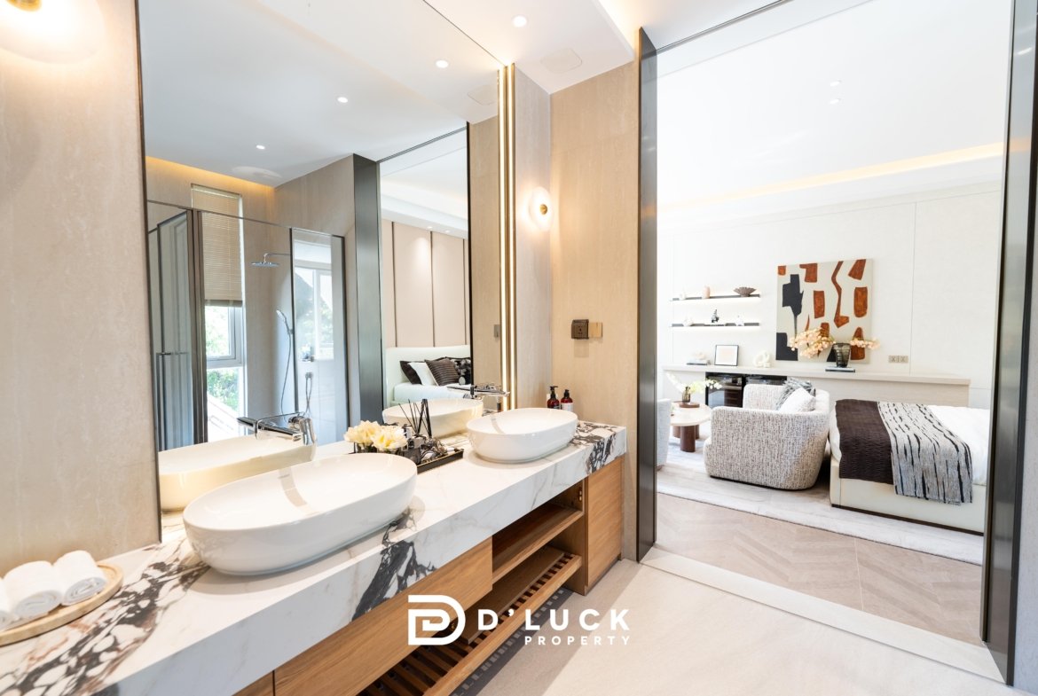 Luxurious bathroom vanity with two round vessel sinks on a marble countertop, mirrored walls, and wood shelving, opening to a stylish living area.