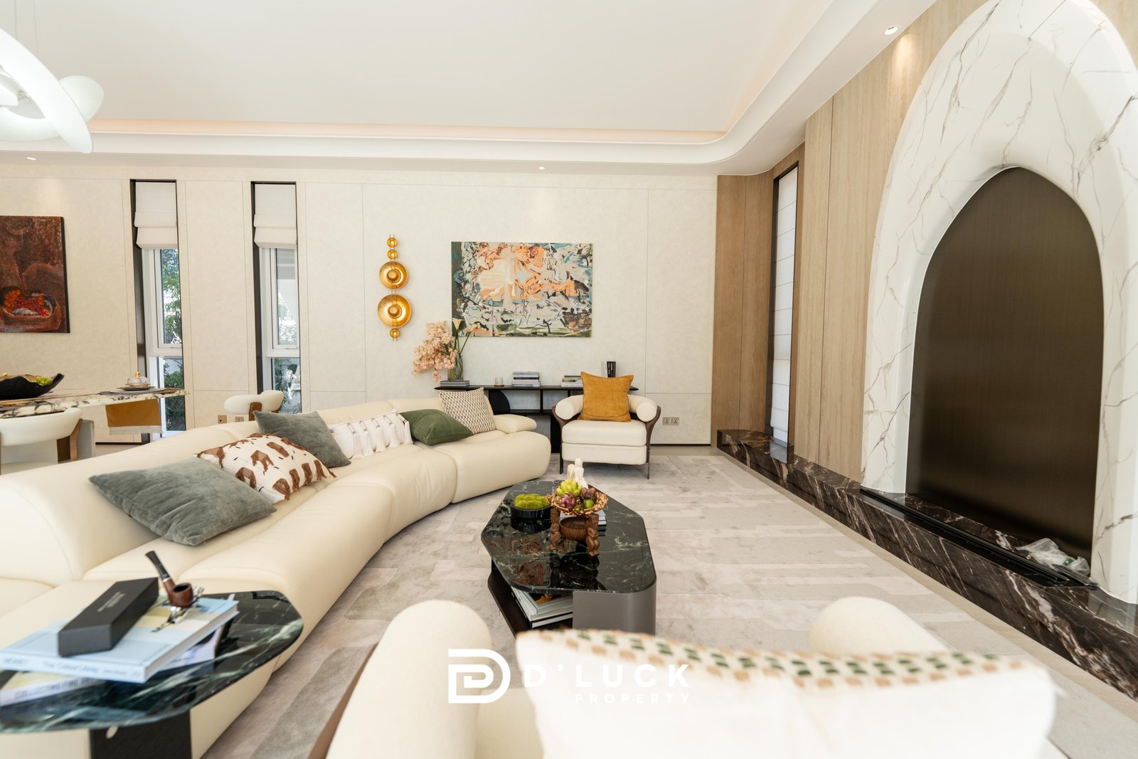 Big_V_Pattaya_Type_A_4 Bright modern living room with a curved white sectional sofa, marble coffee tables, and abstract wall art under soft natural light.