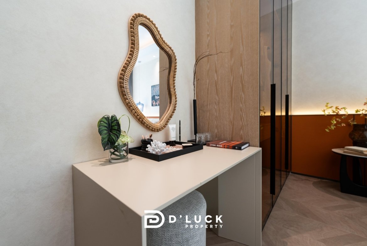Modern office reception: beige desk with a glass vase and small plant, an oval woven mirror on the wall, and branding reading 'D Lucky Property' at the front.