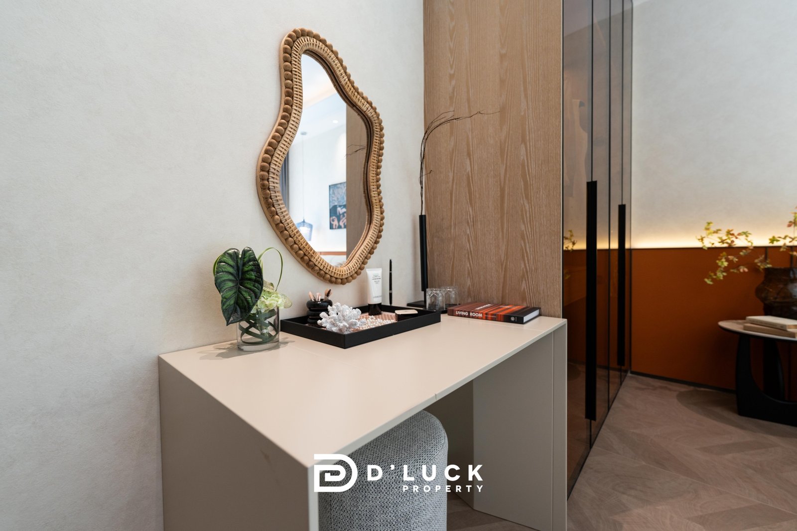 Big_V_Pattaya_Type_A_82 Modern office reception: beige desk with a glass vase and small plant, an oval woven mirror on the wall, and branding reading 'D Lucky Property' at the front.
