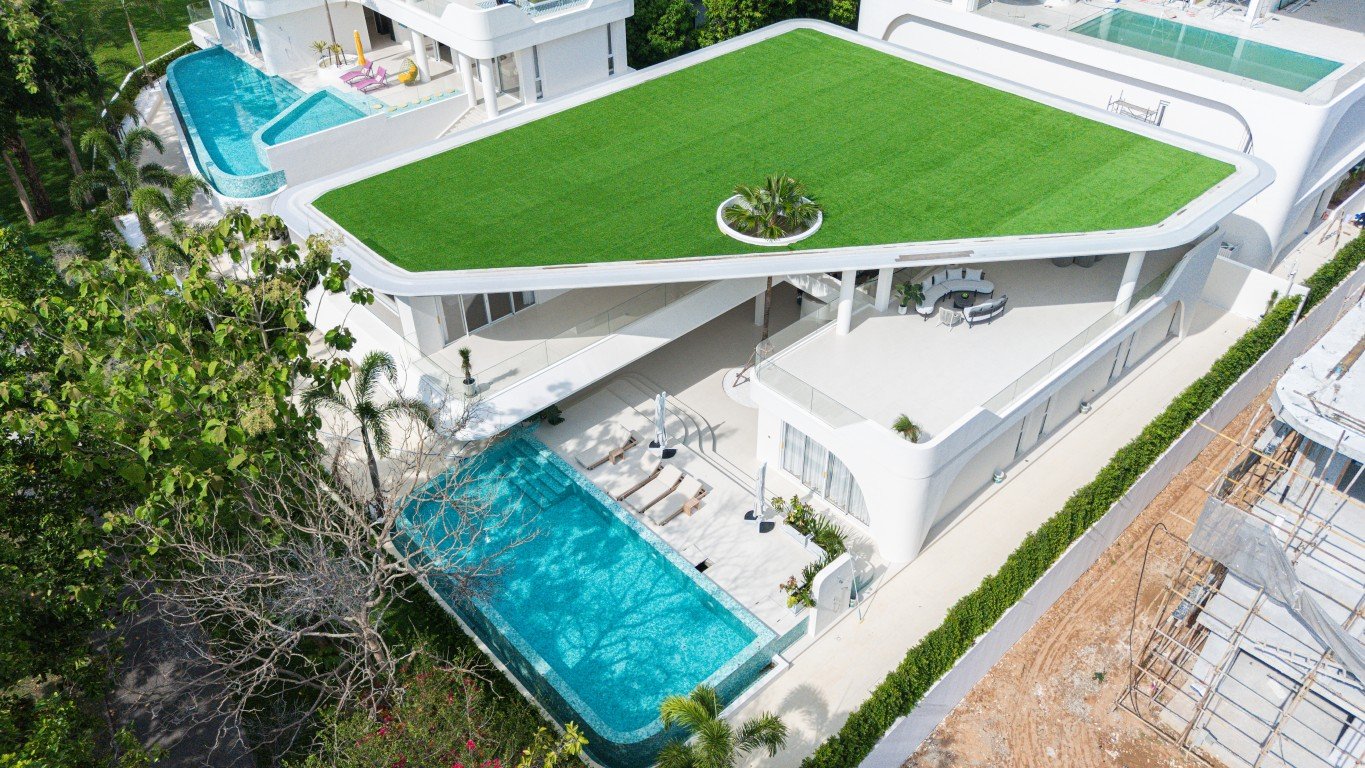 Big_V_Pattaya_Type_B Aerial view of a modern white villa with a green rooftop lawn, circular planter, and turquoise pool nearby.