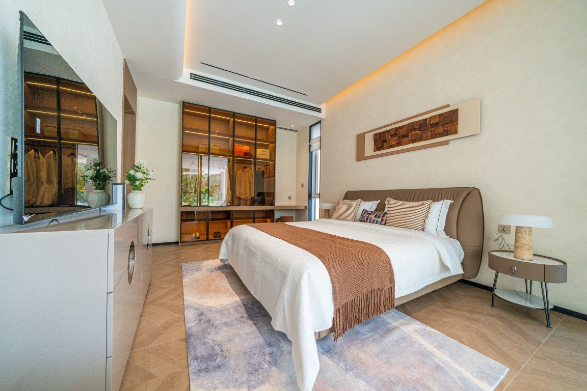Modern hotel bedroom with king bed, white linens, brown throw, and matching nightstands on a light rug.