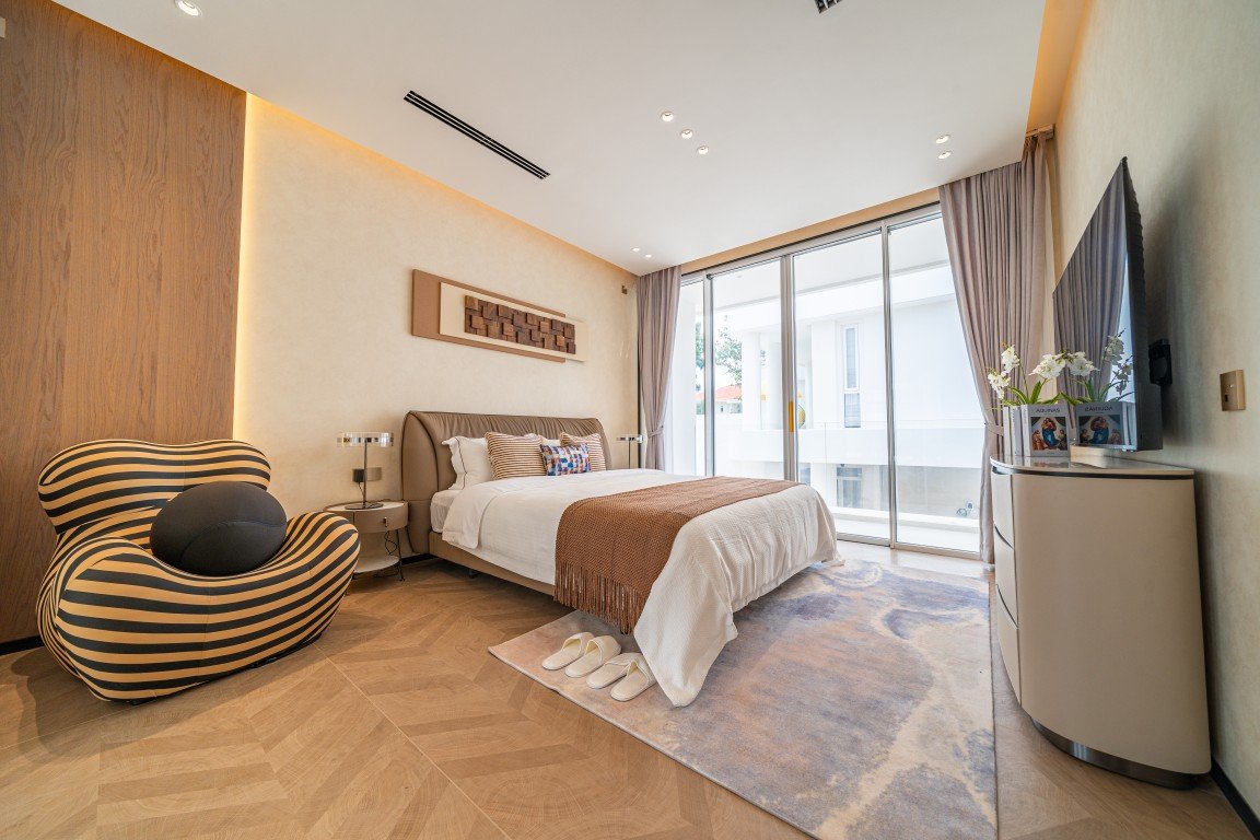 Modern hotel bedroom with a queen bed, brown throw, striped accent chair, and glass balcony doors outlet to natural light.