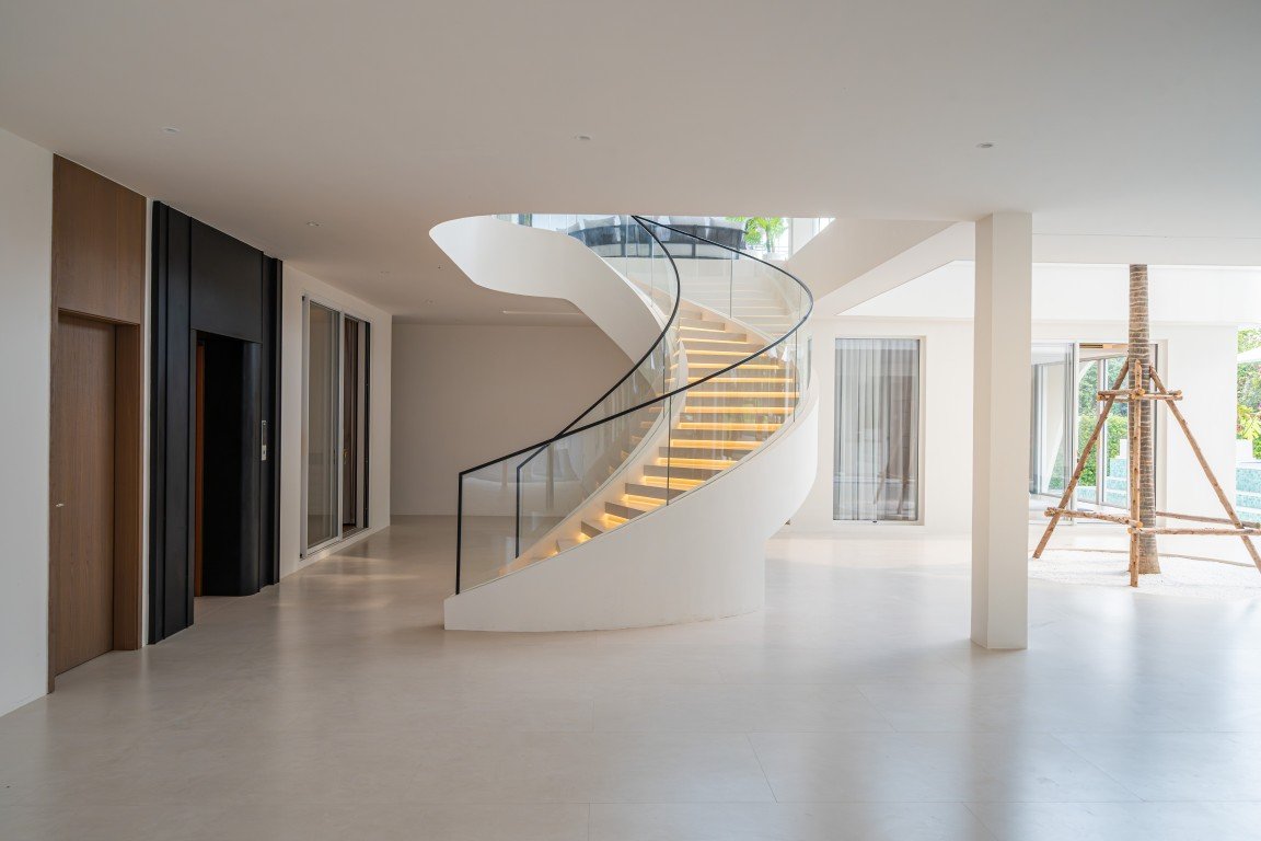 White modern interior with a curved spiral staircase and glass railing in an open, sunlit space.