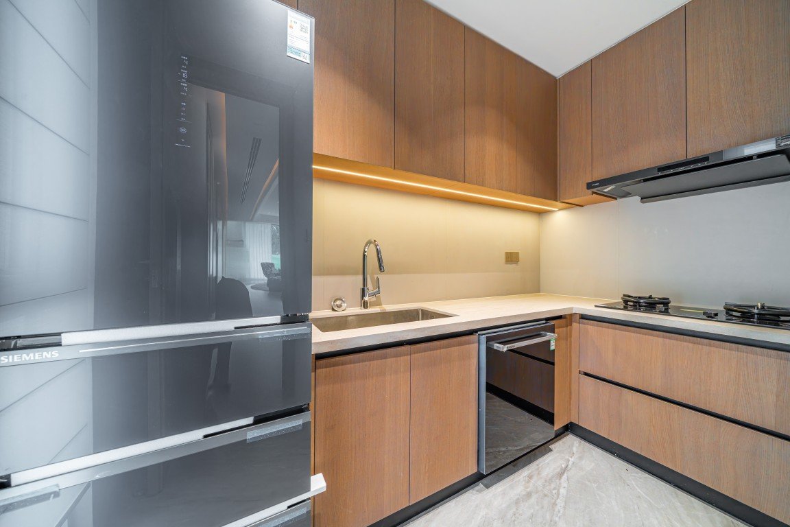 Modern L-shaped kitchen with wooden cabinets, beige countertop, and built-in appliances including a Siemens refrigerator and gas cooktop.