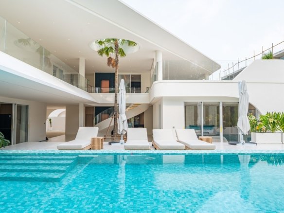 Luxurious white hotel villa with a turquoise swimming pool and row of white lounge chairs on a pool deck under a clear sky