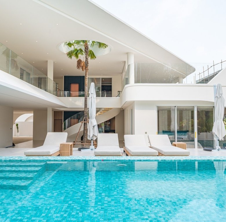 Luxurious white hotel villa with a turquoise swimming pool and row of white lounge chairs on a pool deck under a clear sky