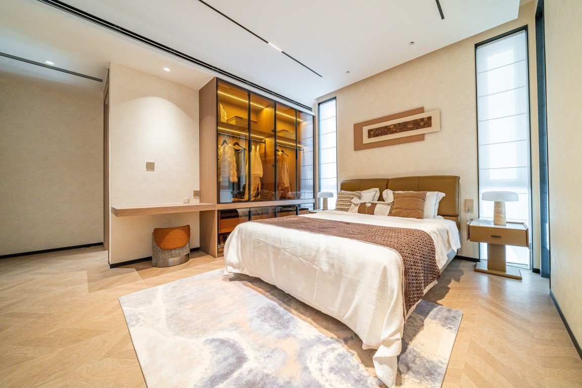 Modern bedroom with a padded headboard bed, glass-front wardrobe, and two bedside tables in neutral tones.